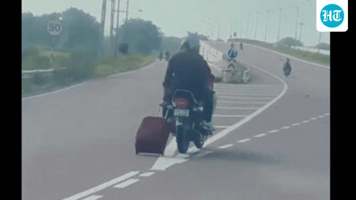 pillion-rider-pulls-trolley-bag-behind-transferring-bike-on-freeway,-web-surprised.-video
